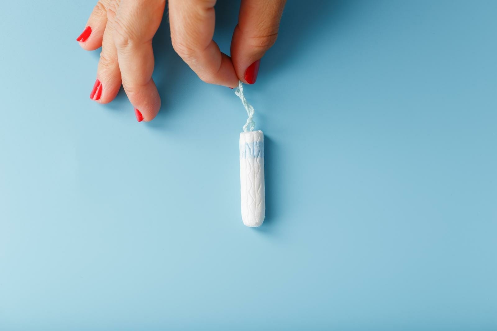 Un tampon hygiénique féminin dans sa main sur un fond bleu avec un espace libre. Cycle menstruel